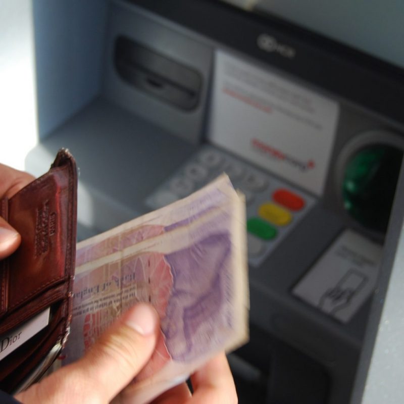 Man withdraws cash from a cash machine and puts it into his wallet.