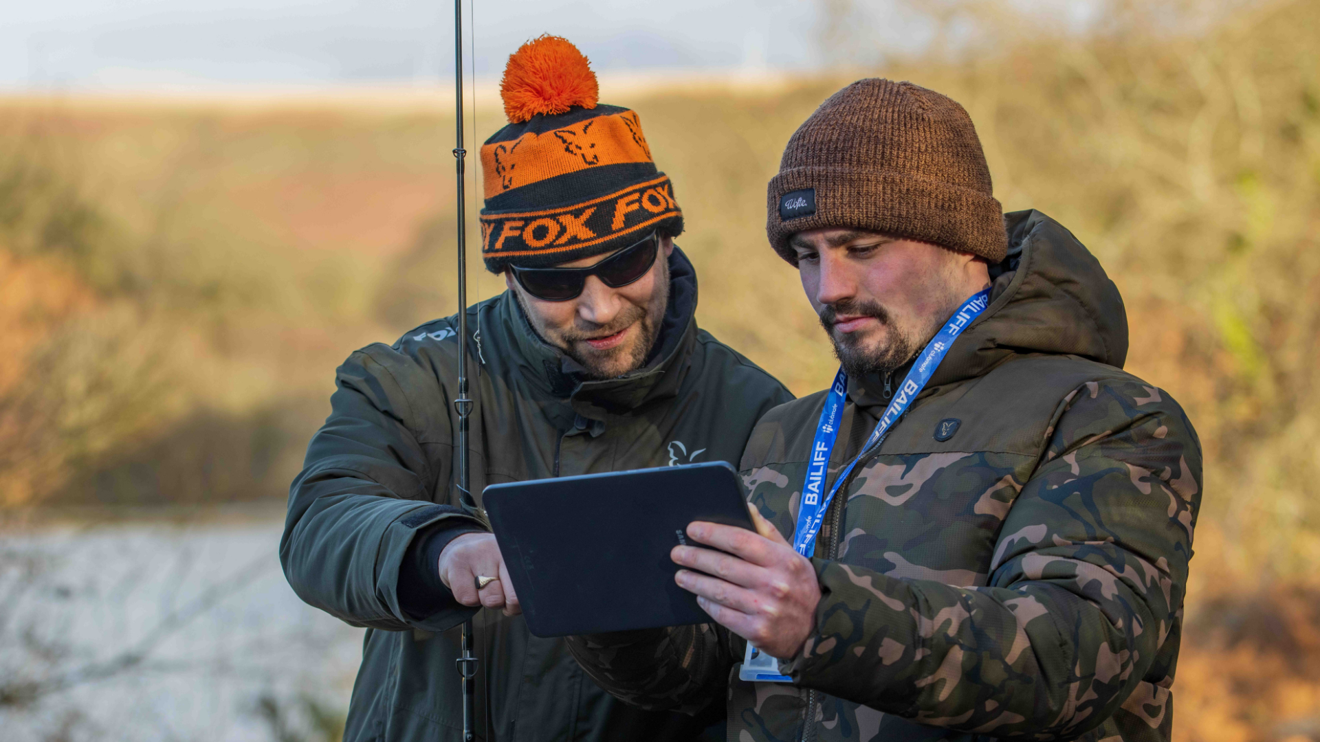 Two anglers looking at an ipad on the riverside with rod in hand. 